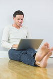 Casual cheery man leaning against wall using laptop