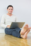 Casual lucky man leaning against wall using laptop