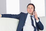 Serious handsome businessman phoning and sitting on couch