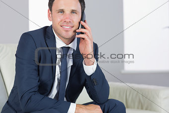 Smiling handsome businessman phoning and sitting on couch