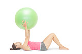 Attractive sporty brunette lying on floor holding exercise ball