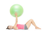 Smiling sporty brunette lying on floor holding exercise ball