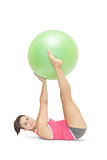 Content sporty brunette lying on floor holding exercise ball between legs