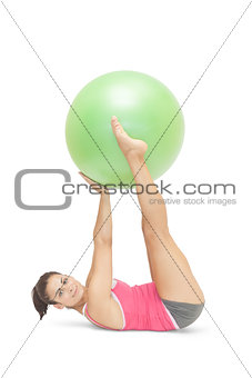 Content sporty brunette lying on floor holding exercise ball between legs