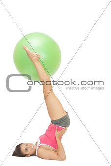 Smiling sporty brunette holding exercise ball between legs