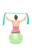 Sporty brunette stretching with resistance band sitting on exercise ball