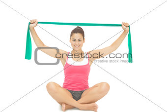Pretty sporty brunette stretching with resistance band sitting cross legged
