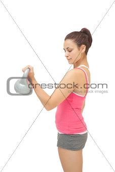 Peaceful sporty brunette holding grey and pink kettlebell