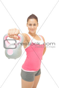 Smiling sporty brunette showing grey and pink kettlebell
