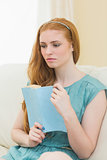 Thoughtful redhead holding a book on the sofa