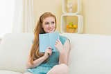 Thoughtful redhead holding a book on the sofa and smiling