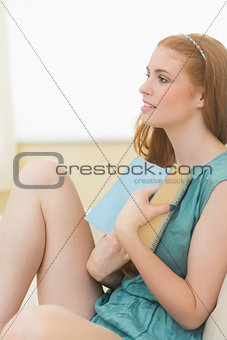 Thinking redhead holding a book on the sofa and smiling