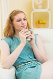 Thoughtful redhead sitting on the couch and holding mug