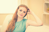 Thoughtful redhead sitting on the couch smiling at camera