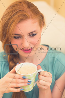 Smiling redhead sitting on the couch having coffee