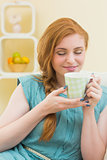 Smiling redhead sitting on the couch smelling coffee