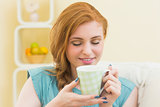 Happy redhead sitting on the couch smelling coffee