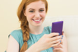 Smiling redhead sitting on the couch using smartphone