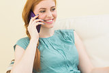Smiling redhead sitting on the couch making a call