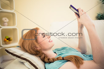 Happy redhead lying on the couch sending a text