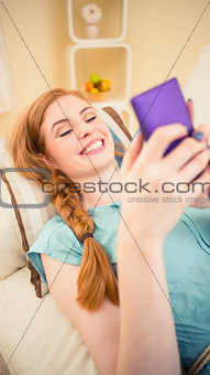 Smiling redhead lying on the couch sending a text