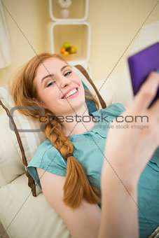Happy redhead lying on the couch sending a text message