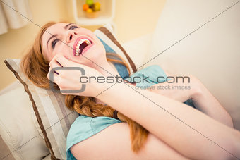 Laughing redhead lying on the couch on the phone