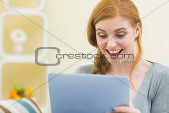 Surprised redhead sitting on the couch using tablet