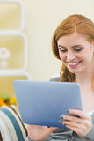 Cheerful redhead sitting on the couch using tablet