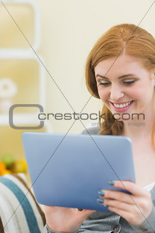 Cheerful redhead sitting on the couch using tablet