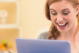 Laughing redhead sitting on the couch using tablet pc