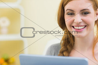 Happy redhead sitting on the couch using tablet pc