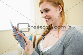 Happy redhead sitting on the couch holding tablet pc