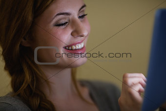 Cheerful redhead sitting on the sofa holding tablet pc at night