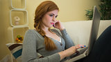 Pretty redhead sitting on the sofa using her laptop at night