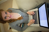 Pretty redhead sitting on the sofa using her laptop at night smiling at camera