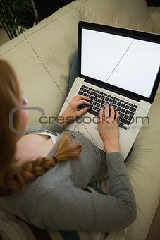 Redhead sitting on the sofa using her laptop at night