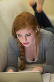 Relaxed redhead lying on the couch using her laptop at night