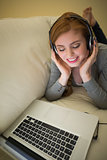 Happy redhead lying on the sofa with her laptop listening to music