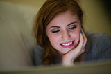Smiling redhead lying on the couch looking at laptop