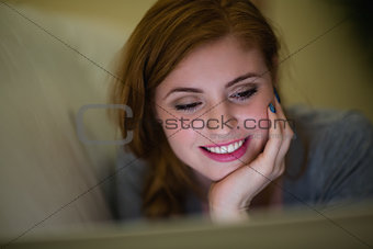 Smiling redhead lying on the couch looking at laptop