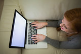 Redhead lying on the couch using her laptop
