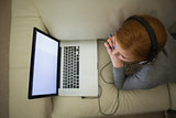 Redhead lying on the couch using her laptop wearing headphones
