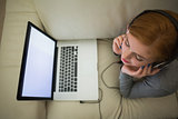 Redhead lying on the couch with her laptop wearing headphones