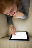 Happy redhead lying on the couch using her tablet pc