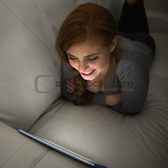 Smiling redhead lying on the couch using her tablet pc