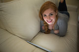 Cheerful redhead lying on the couch using her tablet pc