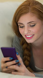 Cheerful redhead lying on the couch sending a text