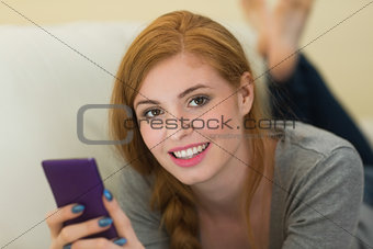 Pretty redhead lying on the sofa sending a text smiling at camera