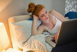 Pretty redhead lying on her bed using laptop